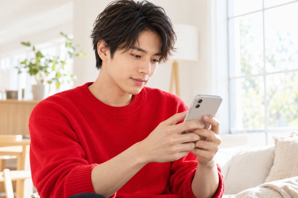 男性が窓際でスマホを持ち、アプリの画面で配信の条件を確認している