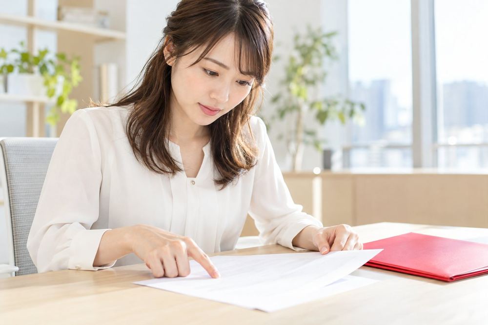 女性が机で、契約書の報酬の項目を指でなぞりながら読んでいる