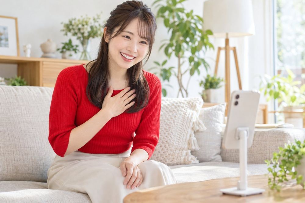 女性がソファに座り、スマホで配信しながら、画面の向こうの視聴者に丁寧にお礼を伝えている