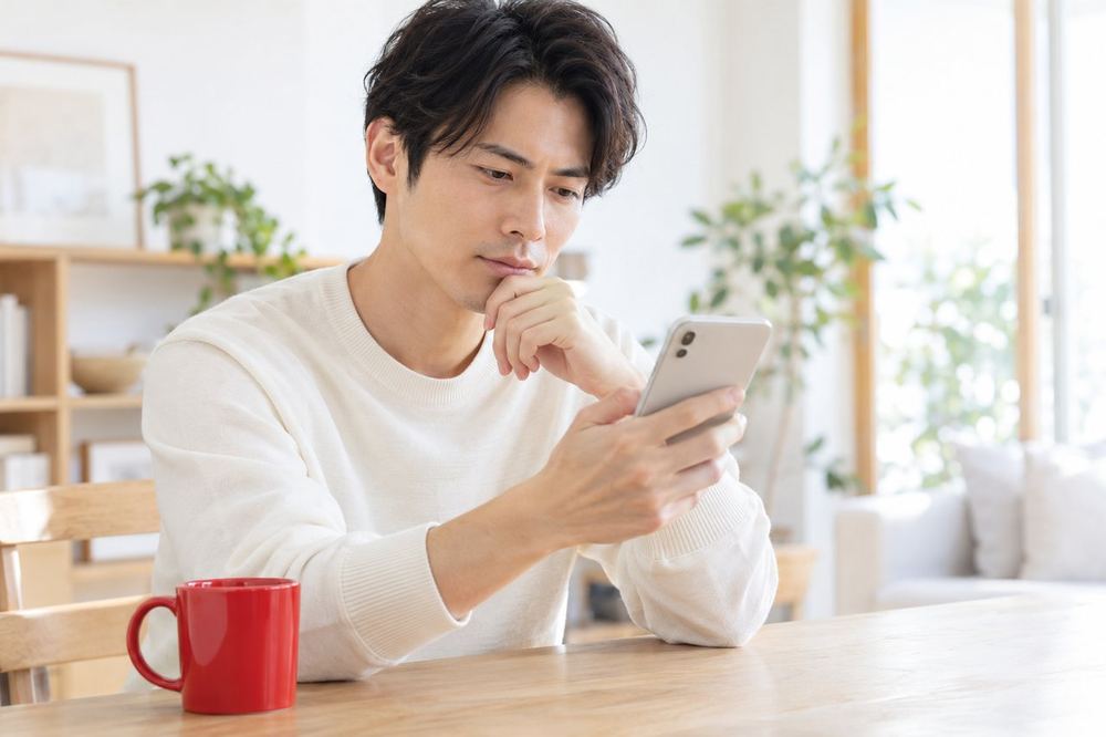 男性が机でスマホの画面を自分の方に向け、報酬の表示を見ながら静かに考えこんでいる
