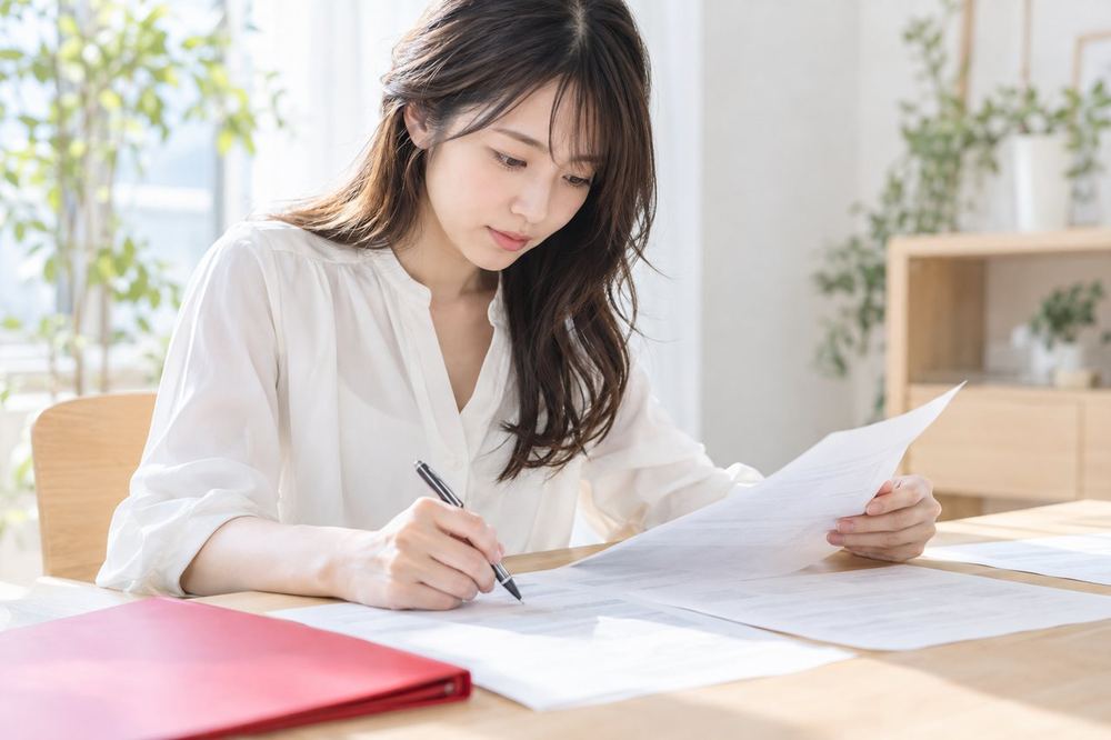 20代の女性が机で契約書の資料を広げ、ペンで気になる箇所に印をつけながら読んでいる