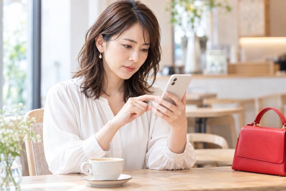 30代の女性がカフェの席で、スマホのDMの内容を見ながら、気になる部分を一つずつ確かめている