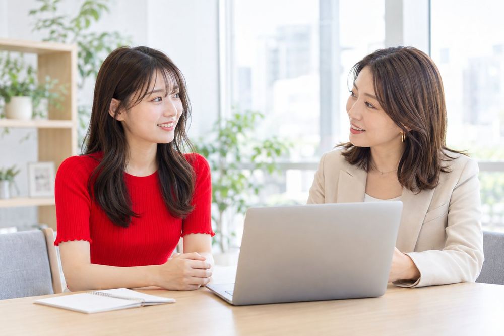 明るい打ち合わせスペースで、マネージャーと配信の進め方について話している20代の女性
