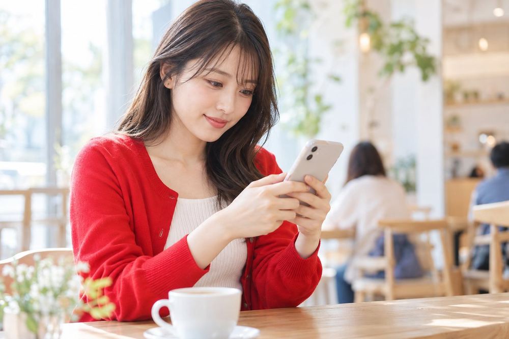 20代の女性がカフェでスマホのメッセージ画面を開き、イベントについて誰かに質問を打ち込んでいる